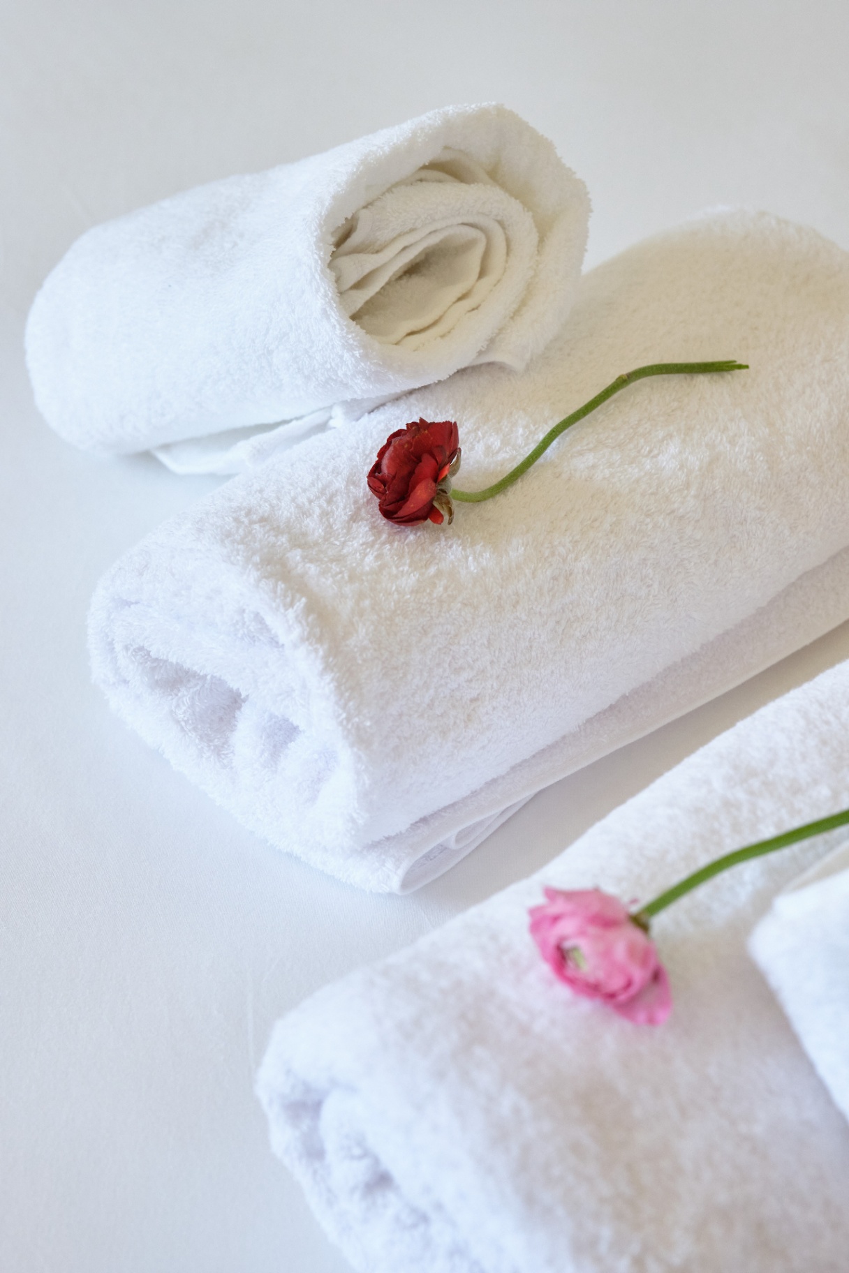 Plush white towels rolled and folded with fresh red and pink ranunculus blooms.