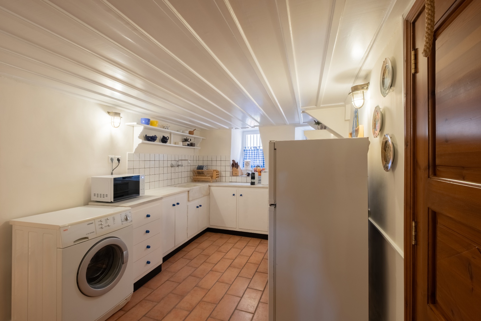 Country kitchen with terracotta floor, white cabinetry, and beamed ceiling.