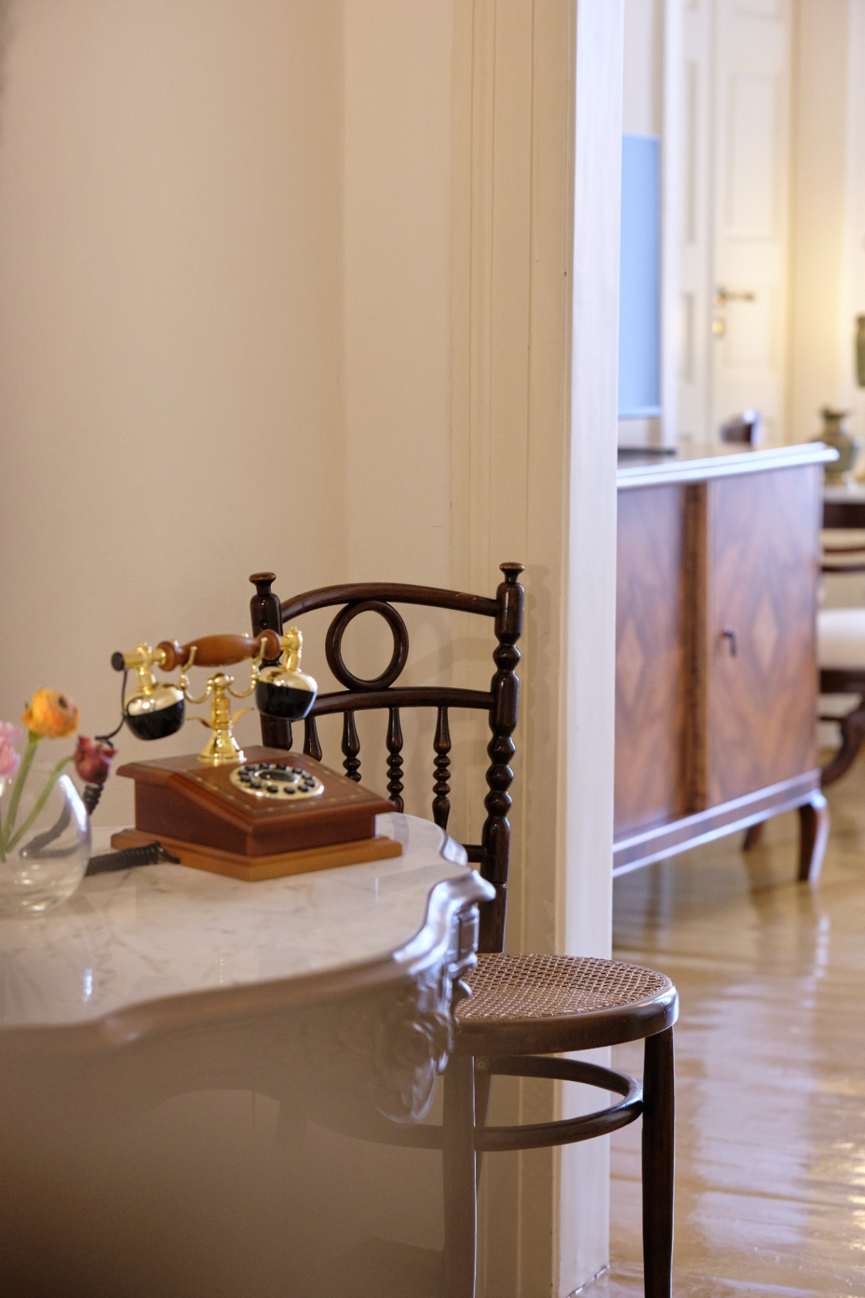 Vintage rotary telephone on a marble console glimpsed past a bentwood cane chair toward a sunlit room.