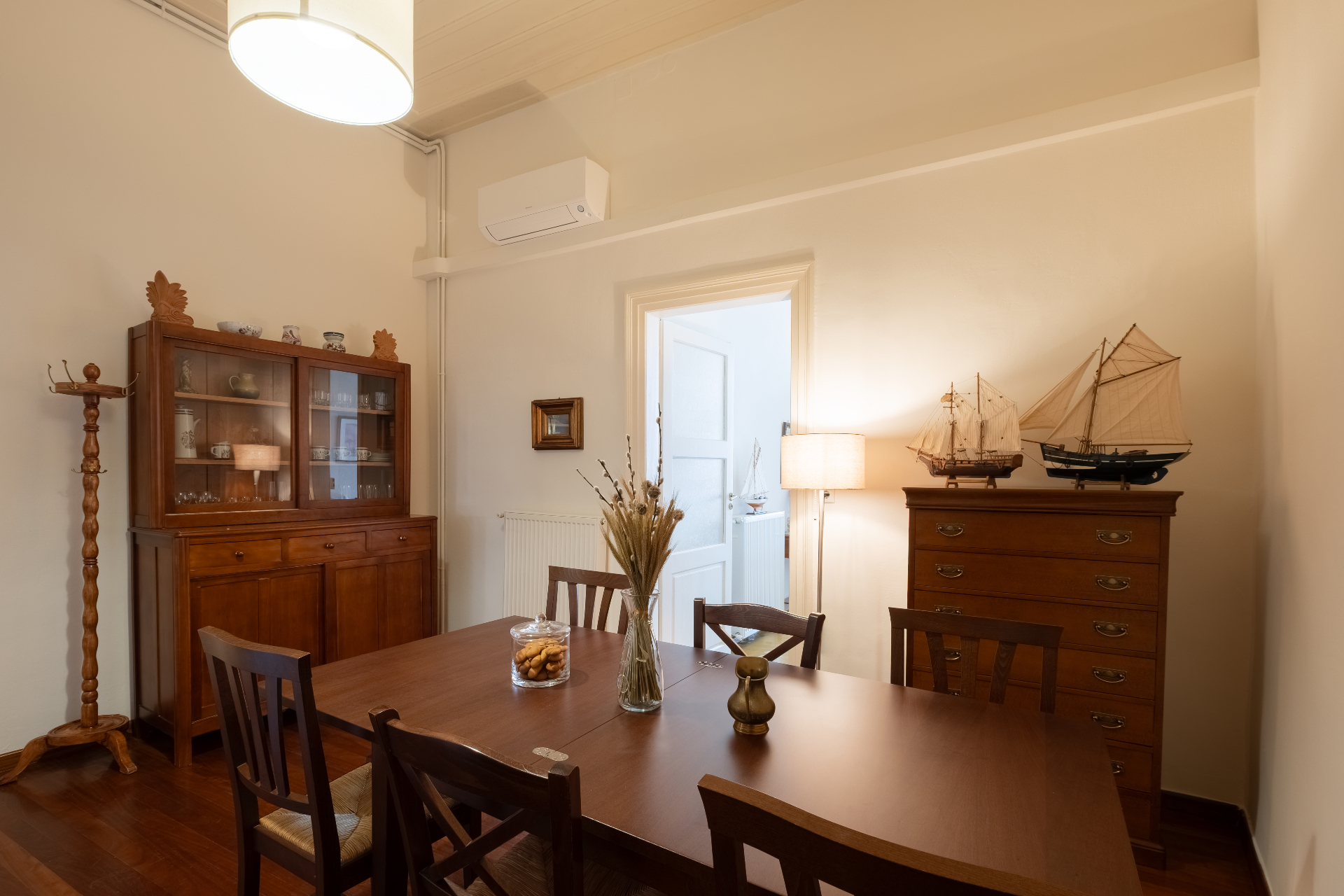 Formal dining room with vintage china cabinet, model sailing ships, and a wooden table set for guests.