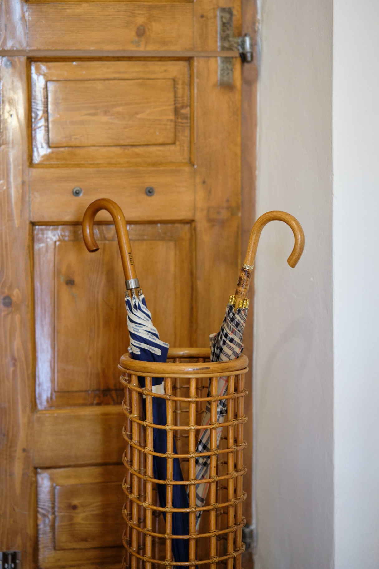 A pair of wood-handled umbrellas in a woven rattan stand beside a warm pine paneled door.