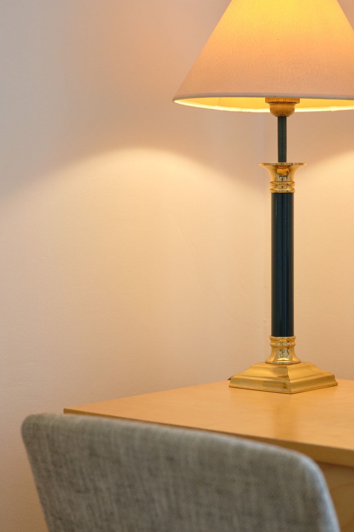 Brass and dark-green column table lamp with a cream shade casting warm light on a pale wall.