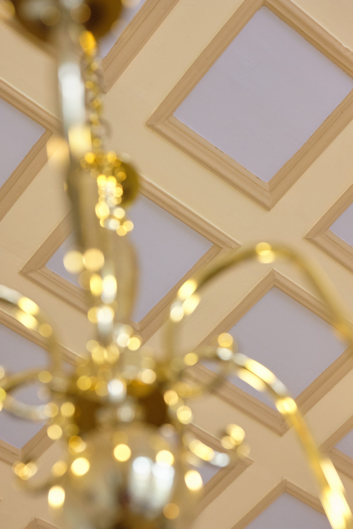 Brass chandelier glinting beneath a painted coffered ceiling with diamond moldings.