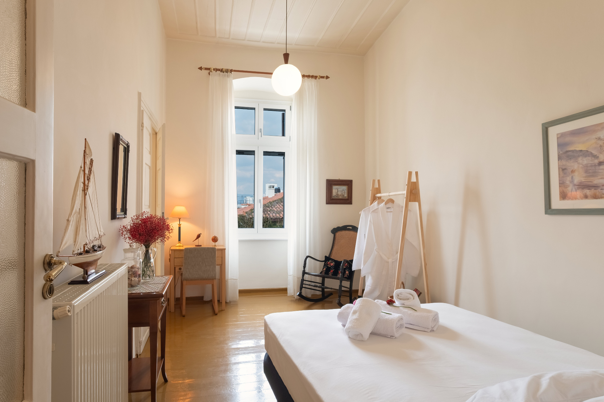Bedroom with white linens, writing desk, and view toward the sea-facing windows.