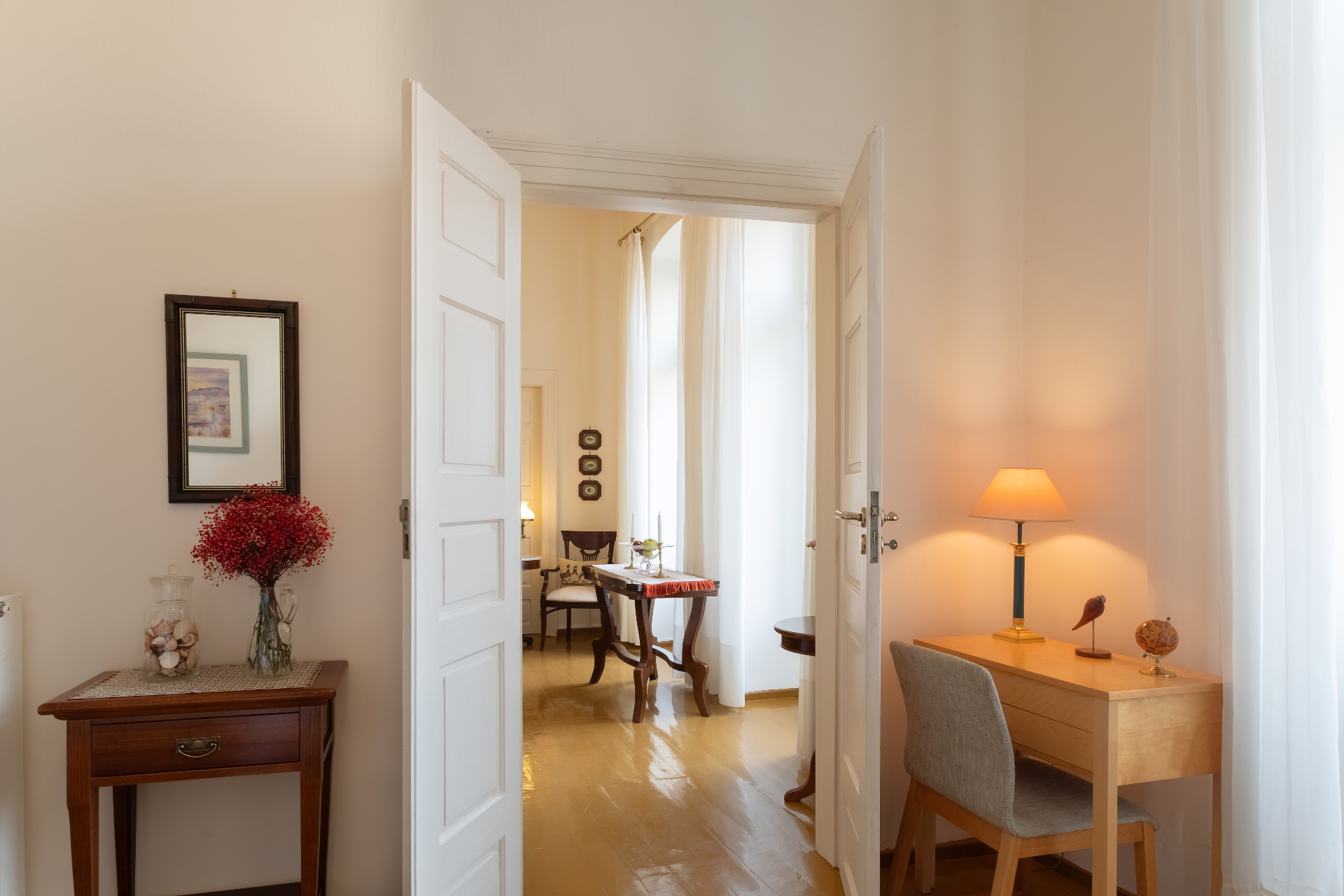 Interior view across rooms with a writing desk and soft evening light.