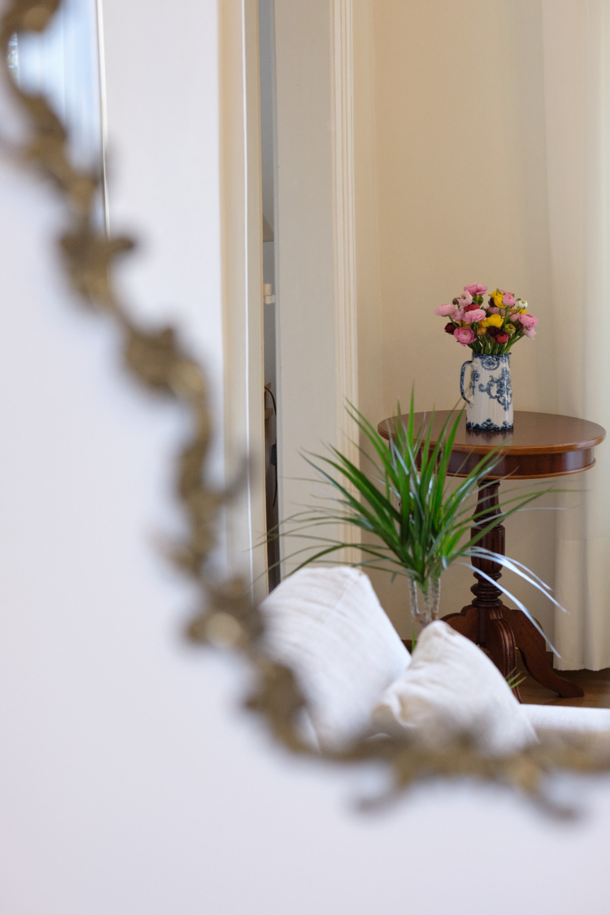 Glimpse through an antique gilt mirror toward a bouquet of ranunculus on a mahogany side table.