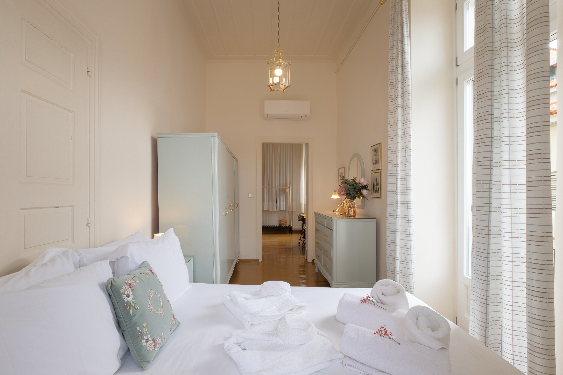 Bright bedroom suite with white linens, mint wardrobe, and high ceilings.