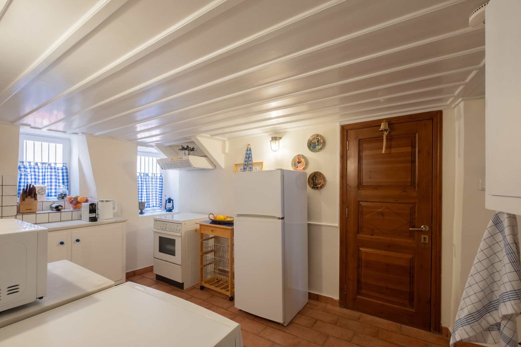 Kitchen with gingham curtains, vintage plates, and full appliances.