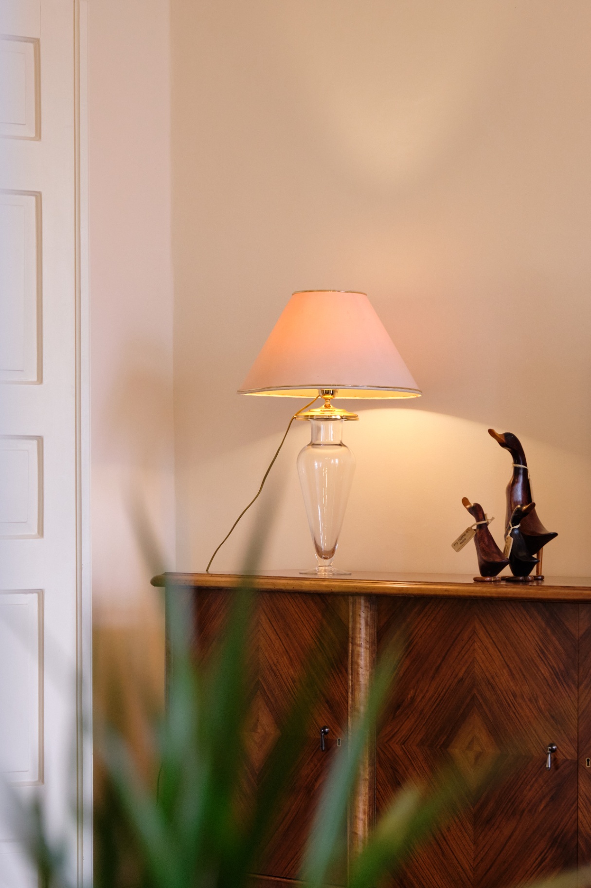 Glass table lamp with rose shade atop an inlaid wooden cabinet with carved duck figurines.