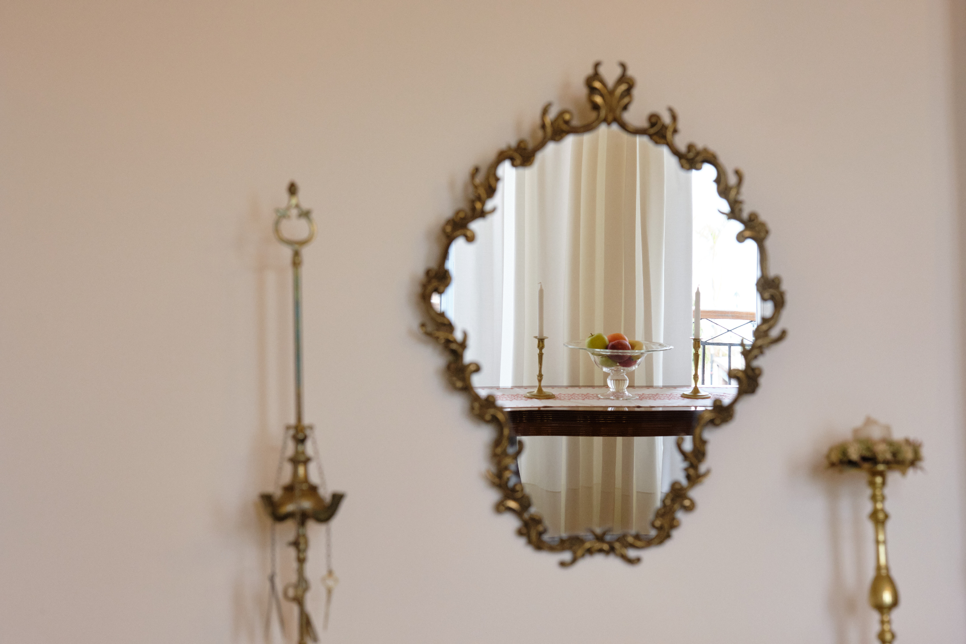 Ornate baroque gilt mirror reflecting a candlelit console with fruit bowl and brass candlesticks.